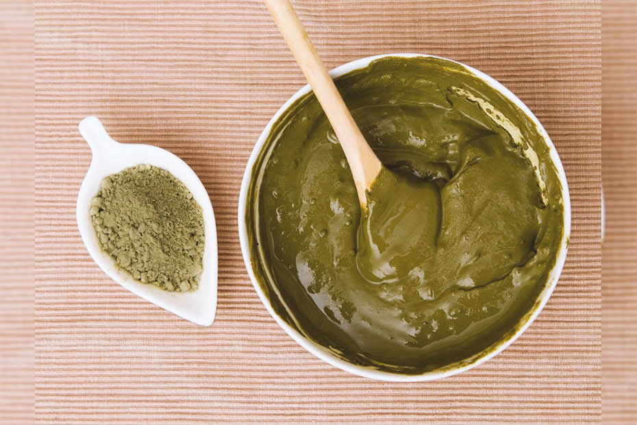 A little plate of powdered henna next to a bowl with a henna mixture and a wooden spoon