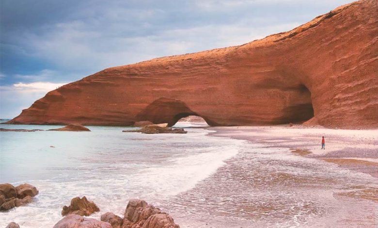 Ochre-coloured rocky arch on a wild beach of Sidi Ifni, Morocco, called Legzira Beach.