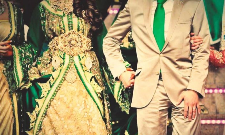A young bride wearing a green Moroccan caftan and is holding the hand of her husband who is wearing a tuxedo with a green tie 
