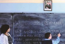 A young Moroccan student writing in Berber on a school blackboard with a Moroccan teacher by his side.