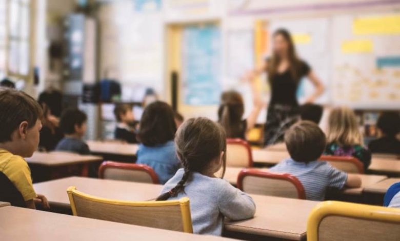 A girl with a braid in a classroom with other children listening to the teacher.