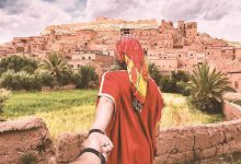 A woman in a red Moroccan gandoura pulling someone's hand to Taourirt Kasbah in Ouarzazate, in Morocco.