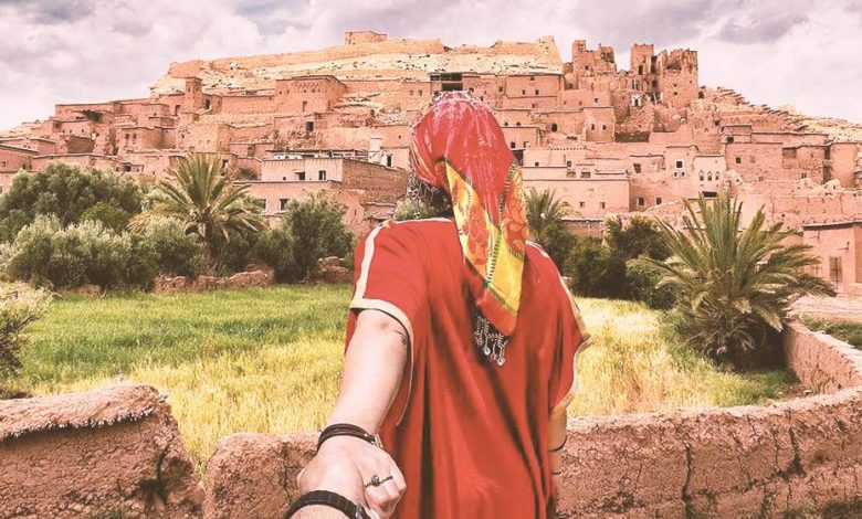 A woman in a red Moroccan gandoura pulling someone's hand to Taourirt Kasbah in Ouarzazate, in Morocco.