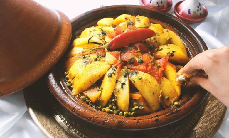 A Moroccan tagine with potatoes, peas, carrots, and tomatoes with a hot pepper on top as decoration.