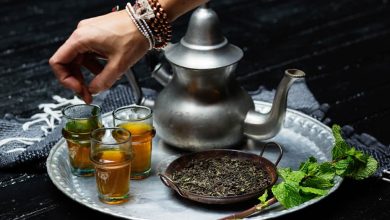 A teapot and three glasses filled with moroccan tea served on a silver footed tea trays.