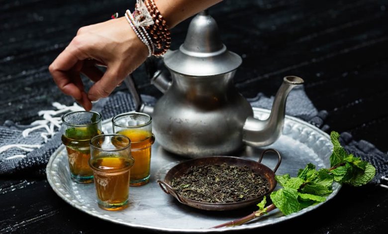 A teapot and three glasses filled with moroccan tea served on a silver footed tea trays.