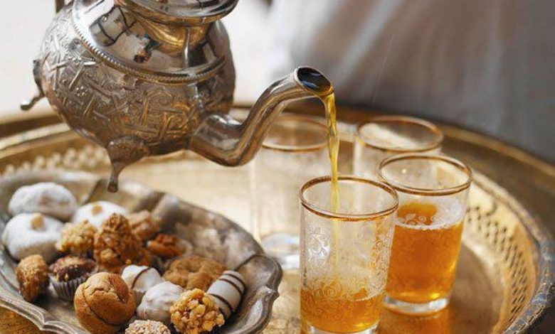 Moroccan teapot pouring tea in a glass next to a plate of Moroccan pastries